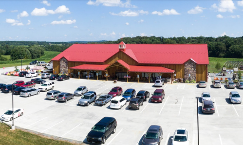 A large wooden building with a red roof and stone accents, surrounded by a parking lot filled with cars.