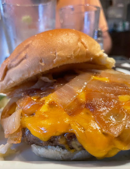 A close-up of a cheeseburger with melted cheese, sautéed onions, and a soft bun on a plate.