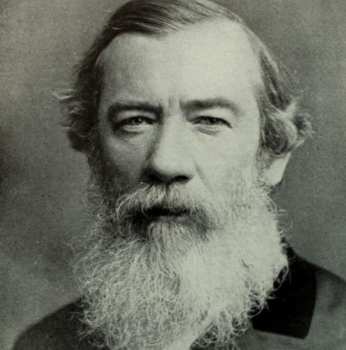 Black and white portrait of a man with a long beard and wavy hair, looking directly at the camera.