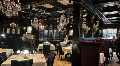 Elegant restaurant interior with dark wood, chandeliers, and white tablecloths, creating a sophisticated dining atmosphere.