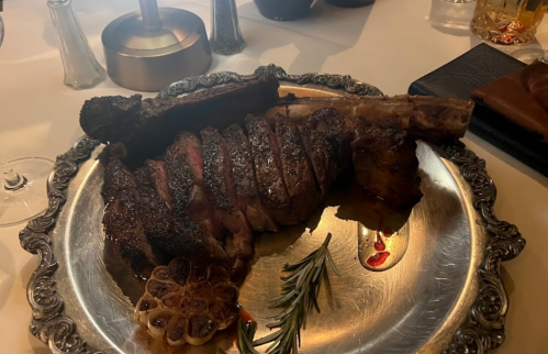 A beautifully plated, sliced steak on a silver platter, garnished with rosemary and roasted garlic.