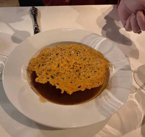 A plate with a crispy, golden-brown cheese crisp resting on a dark, savory sauce.
