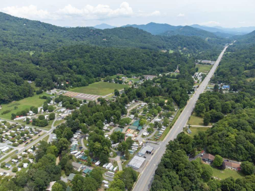 Aerial view of a rural area with mobile homes, fields, and a highway surrounded by green mountains.