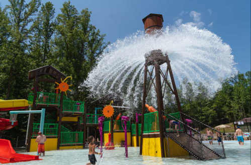 A water park scene with a large water feature, colorful slides, and children playing in the shallow pool.
