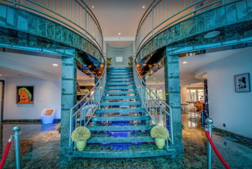 Elegant interior featuring a grand staircase with marble steps and decorative plants, illuminated by soft lighting.
