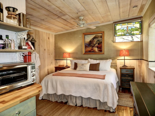 Cozy bedroom with a wooden ceiling, a queen bed, decorative lamps, and a stained glass window.