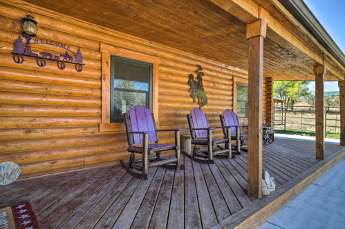 A rustic log cabin porch with three purple rocking chairs and a welcome sign, surrounded by nature.