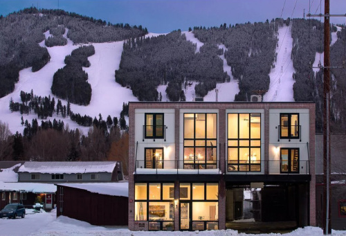 Modern building with large windows in the foreground, snowy mountain slopes in the background at dusk.