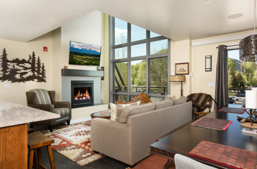 Cozy living room with a fireplace, large windows, and modern decor, featuring a TV and a dining area.