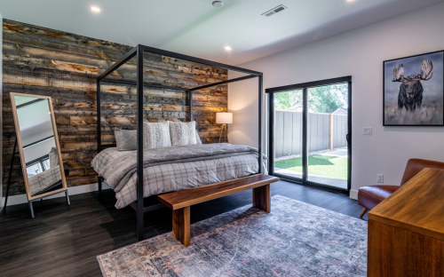 A modern bedroom featuring a four-poster bed, wooden accent wall, and large windows with a view of the outdoors.