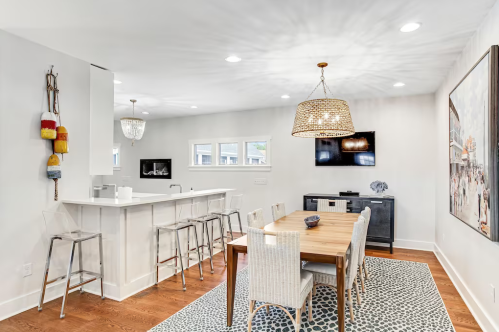 Modern dining area with a wooden table, white chairs, bar seating, and stylish lighting in a bright, open space.