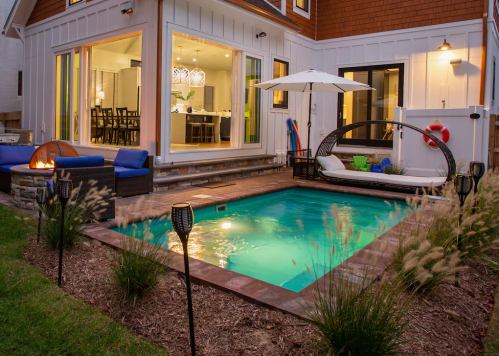 A cozy backyard with a small pool, lounge chairs, and a fire pit, surrounded by greenery and modern outdoor decor.