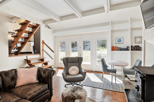 Cozy living room with a leather sofa, modern chair, dining table, and large windows overlooking a green yard.