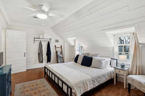 Cozy bedroom with a sloped ceiling, featuring a bed, nightstand, and natural light from two windows.