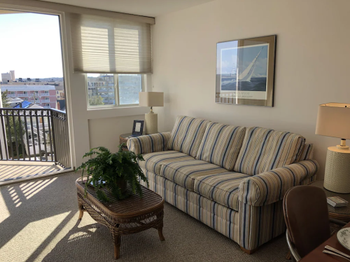 A cozy living room with a striped sofa, a coffee table, a lamp, and a view of the outdoors through a large window.