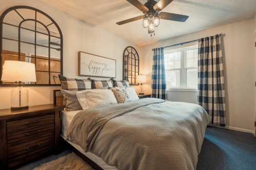 Cozy bedroom with a large bed, decorative pillows, two lamps, and plaid curtains, featuring stylish mirrors on the walls.