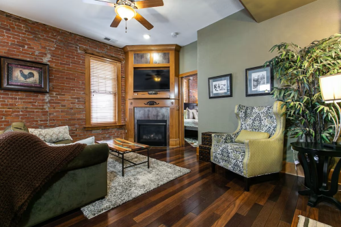 Cozy living room with brick walls, hardwood floors, a fireplace, and stylish furniture, including a green armchair.