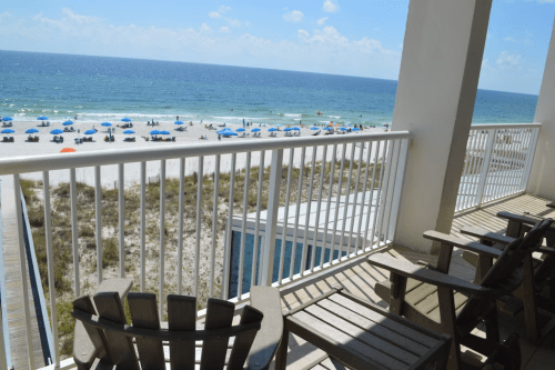 View from a balcony overlooking a beach with umbrellas and chairs, blue ocean, and clear sky.