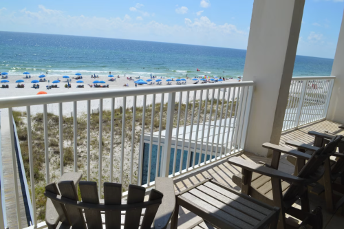 View from a balcony overlooking a beach with umbrellas and chairs, blue ocean, and clear sky.