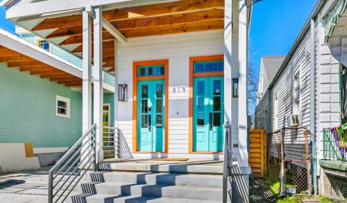 Brightly colored entrance with turquoise doors and a covered porch, surrounded by light-colored buildings and clear blue sky.