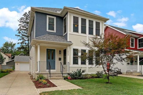 A two-story house with blue and white siding, a front porch, and a landscaped yard on a sunny day.