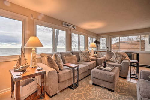 Cozy living room with large windows, soft gray furniture, and a view of the water, featuring warm lighting and decorative accents.