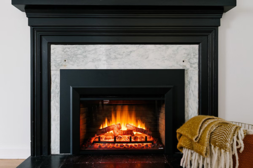 A cozy fireplace with a marble surround, glowing flames, and a warm blanket draped nearby.