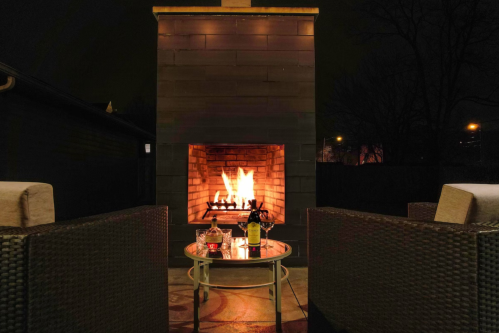 A cozy outdoor fireplace at night, surrounded by wicker chairs and a small table with drinks.