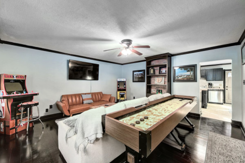 Cozy living room with a shuffleboard table, leather couch, arcade machine, and a TV on the wall.