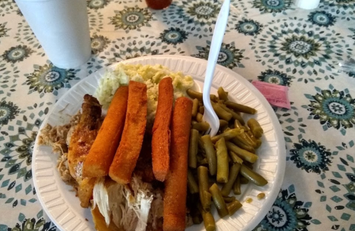 A plate of food featuring fried fish, green beans, coleslaw, and fried okra, with a drink in a cup nearby.