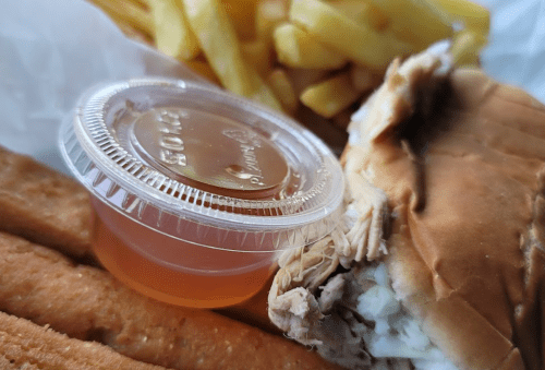 A close-up of a meal featuring a sandwich with chicken, a cup of sauce, and a side of French fries.
