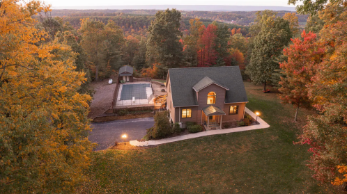 Aerial view of a house surrounded by autumn trees, with a pool and scenic landscape in the background.