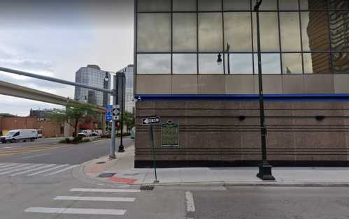 Street view of a city corner with a historical marker, modern buildings, and a traffic signal.