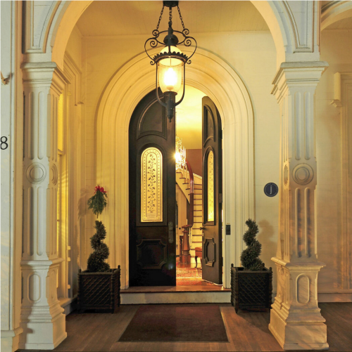A grand entrance with a large wooden door, ornate columns, and warm lighting, leading to a staircase inside.