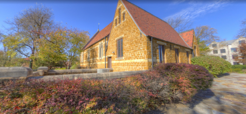 A stone building with a red roof surrounded by colorful foliage and trees under a clear blue sky.