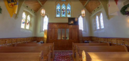 Interior of a church featuring wooden pews, stained glass windows, and a decorative altar area.