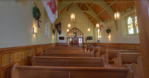 Interior of a church featuring wooden pews, stained glass windows, and decorative flags hanging from the ceiling.