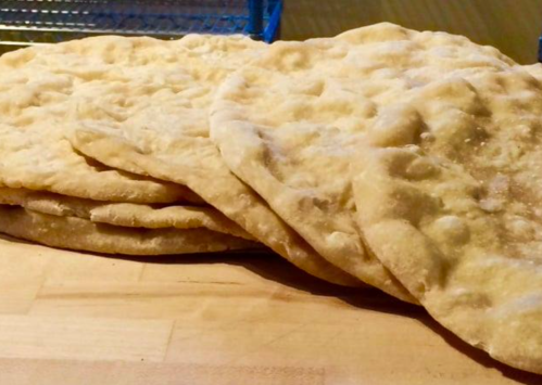 A stack of freshly baked flatbreads on a wooden surface.