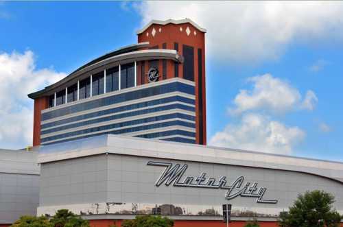 Exterior view of the MotorCity Casino Hotel, featuring a modern design against a blue sky with clouds.