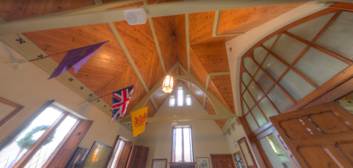 Interior view of a building with a wooden ceiling, flags hanging, and large windows letting in natural light.
