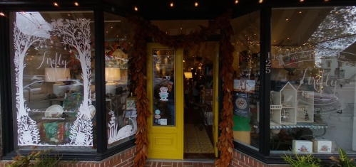 A cozy storefront with a bright yellow door, decorated with autumn leaves and warm lighting, showcasing various items inside.