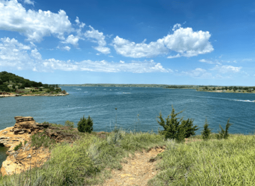 A scenic view of a river surrounded by green hills and blue skies with fluffy clouds.