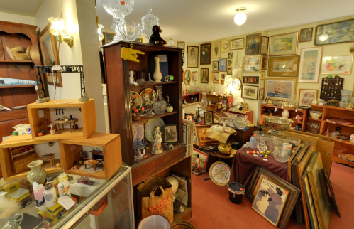 A cozy antique shop filled with various collectibles, glassware, and framed art on the walls.