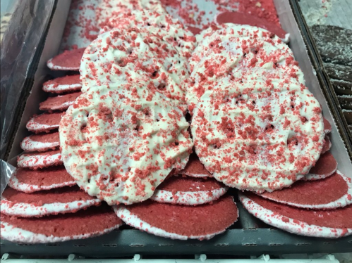 A close-up of red and white cookies topped with sprinkles, arranged neatly on a tray.