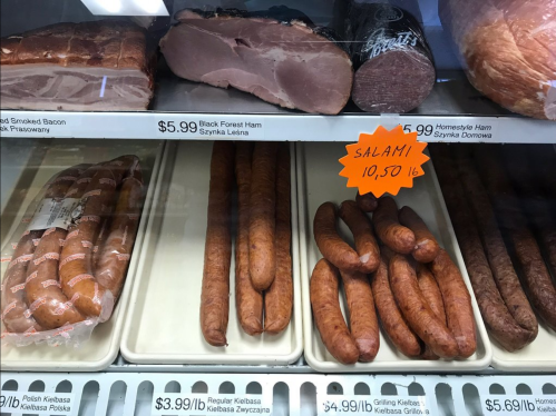 Display case with various meats: smoked bacon, black forest ham, and salami, with price tags visible.
