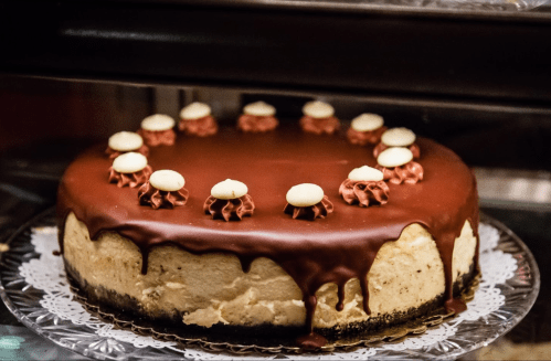 A round chocolate-covered cake with decorative frosting on top, displayed on a lace doily.