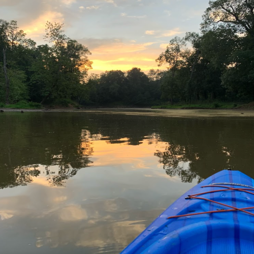 A serene river scene at sunset, with reflections on the water and a kayak in the foreground.