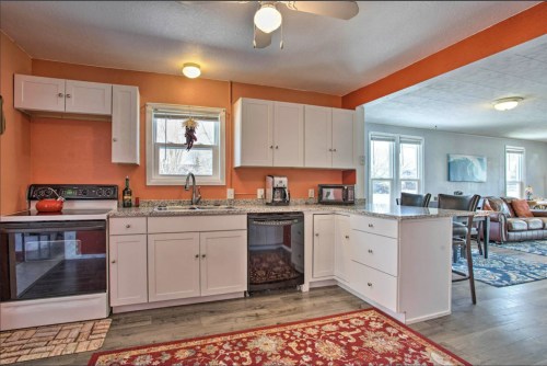 Bright kitchen with white cabinets, granite countertops, and a cozy living area visible in the background.