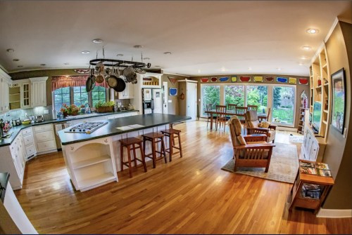 Spacious kitchen with a large island, wooden floors, and a dining area featuring large windows and colorful wall art.