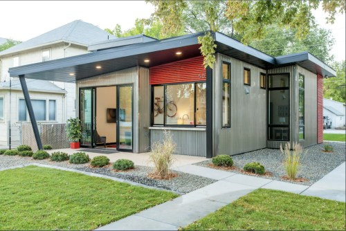 Modern house with a sleek design, large windows, and landscaped yard featuring grass and shrubs.